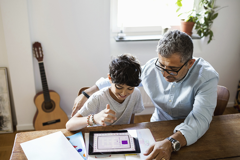 En pappa som sitter vid ett köksbord och hjälper sin son med läxorna.